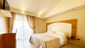 Une chambre d’hôtel avec un grand lit, une tête de lit en bois, un téléviseur à écran plat fixé au mur et un bureau avec une chaise.