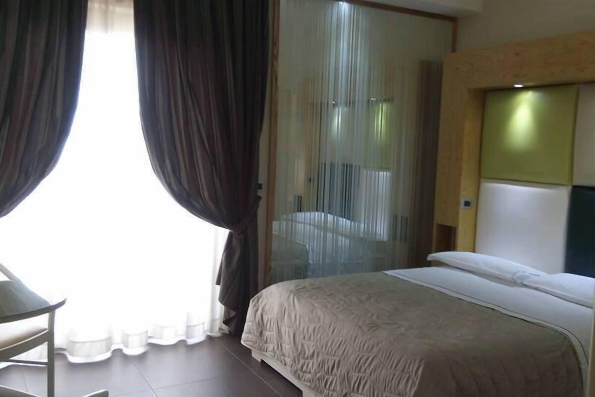 A hotel room with a bed, a chair, and a large window with curtains.