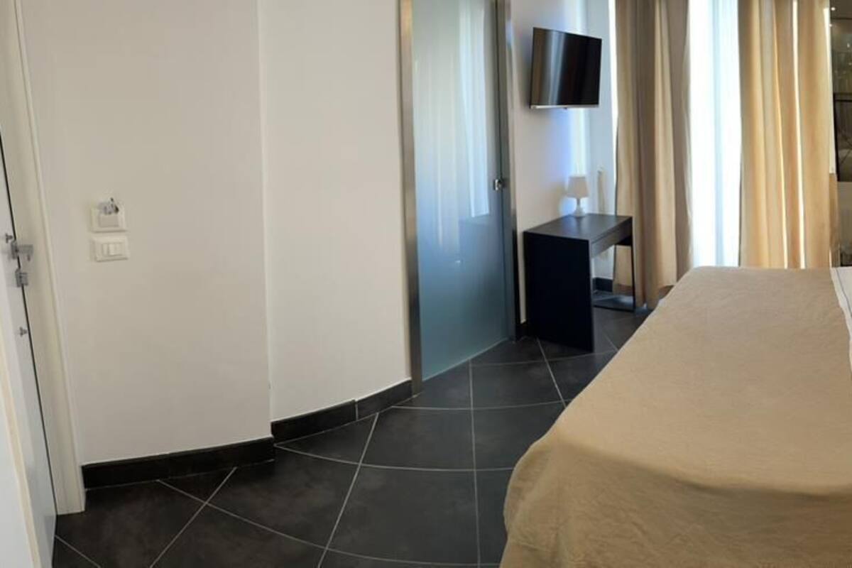 A hotel room with a large bed, a bedside table with a lamp, a TV mounted on the wall, and a small desk.
