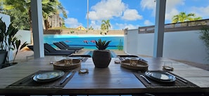 A dining area with a view of a pool, outdoor seating, and tropical plants. - Appartement Mileo Jan Thiel Curacao (Jan Thiel)