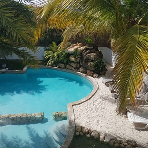 A swimming pool with a sandy edge, surrounded by palm trees and rocks. - Appartement Mileo Jan Thiel Curacao (Jan Thiel)