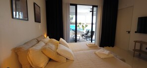 A hotel room with a large bed, a view of a pool and outdoor seating through an open door. - Appartement Mileo Jan Thiel Curacao (Jan Thiel)