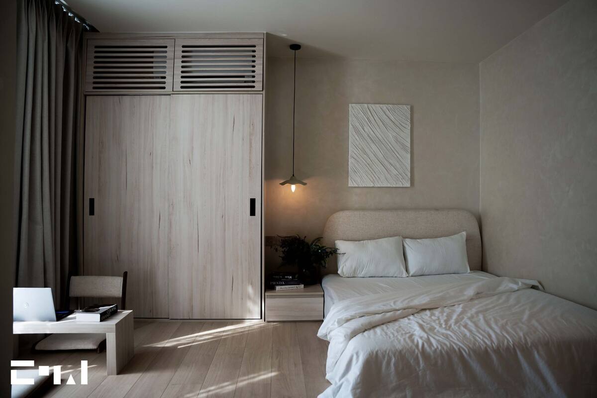 Een moderne slaapkamer met een bed, bureau, stoel, garderobe en hanglamp.