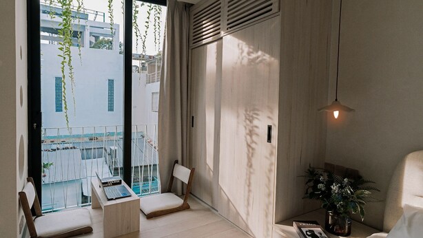 A modern bedroom with a large window, a bed, a chair, a small table, and a bedside plant.