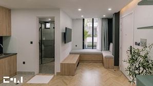 A modern living room with a built-in bench, a TV mounted on the wall, and a sliding glass door leading to a balcony.