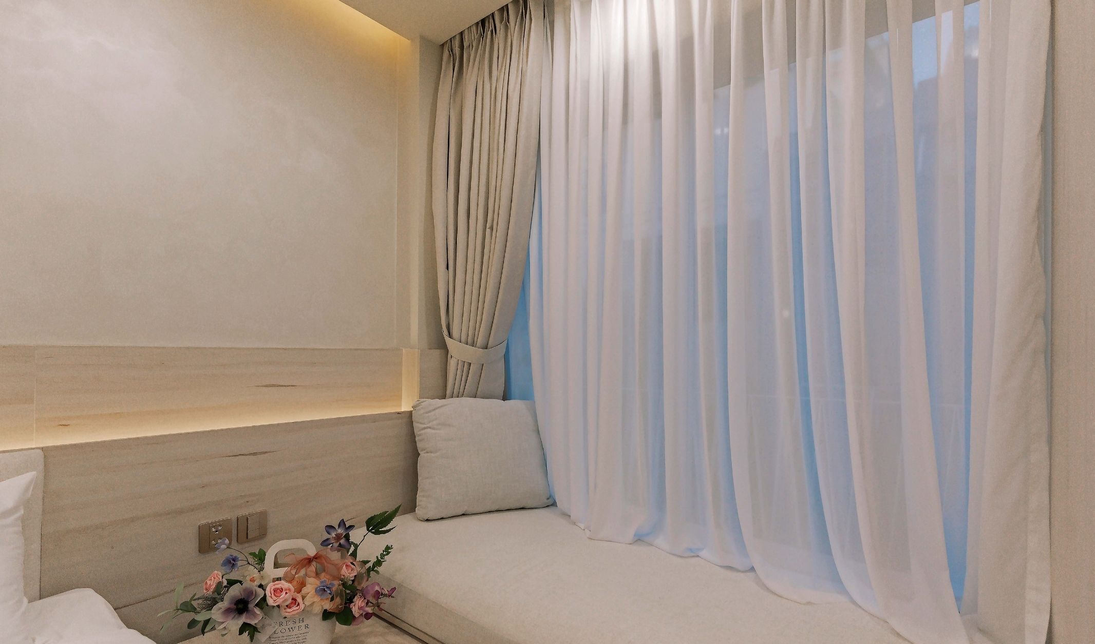 A hotel room with a bed, a bedside table, a lamp, and a floral arrangement.