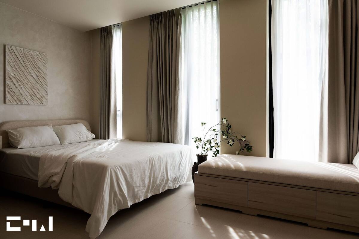 Een moderne slaapkamer met een groot bed, een kleinere bank en een potplant.
