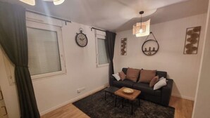 A living room with a sofa, a coffee table, a clock, and a window with curtains.