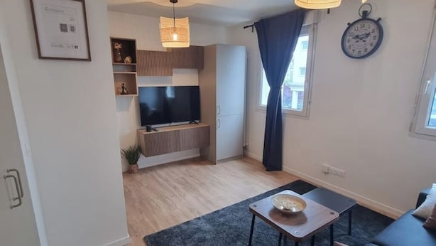 A modern living room with a flat-screen TV, a sofa, a coffee table, and a clock on the wall.