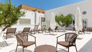 Un área de estar al aire libre con sillas y mesas, sombrillas y un edificio con un muro de azulejos y una cruz.