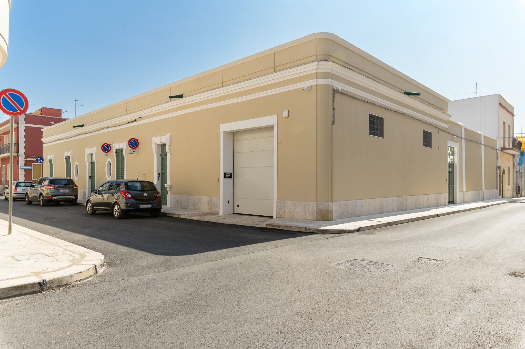 Un edificio beige con una porta e finestre bianche, auto parcheggiate e un segnale di divieto di sosta.