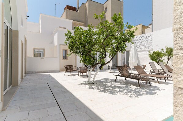 A courtyard with white tiled flooring, a tree, and several lounge chairs.