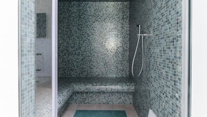 Ein kleiner, abgeschlossener Duschbereich mit mosaikbesetzter geflieste Wand und einer Sitzbank.