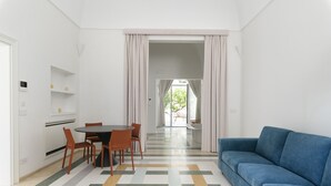 A modern living room with a blue sofa, a dining area with a table and chairs, and a view through a doorway to an outdoor seating area. - Hydeout Luxury Suite - Botte 14 by Wonderful Italy (San Vito dei Normanni)