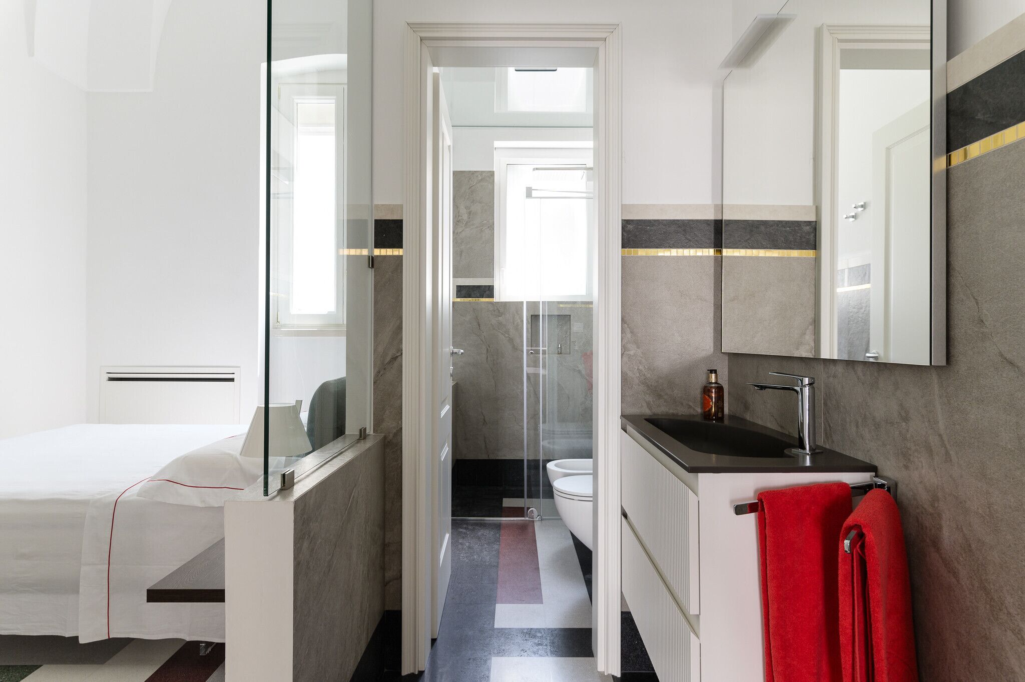 A modern bathroom with a glass shower enclosure, a white toilet, and a black sink with a red towel.