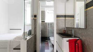 A modern bathroom with a glass shower enclosure, a white toilet, and a black sink with a red towel.