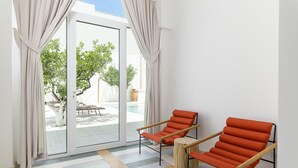 A room with two orange chairs, a patterned rug, and a sliding glass door leading to an outdoor area with a pool and trees. - Hydeout Luxury Suite - Botte 14 by Wonderful Italy (San Vito dei Normanni)
