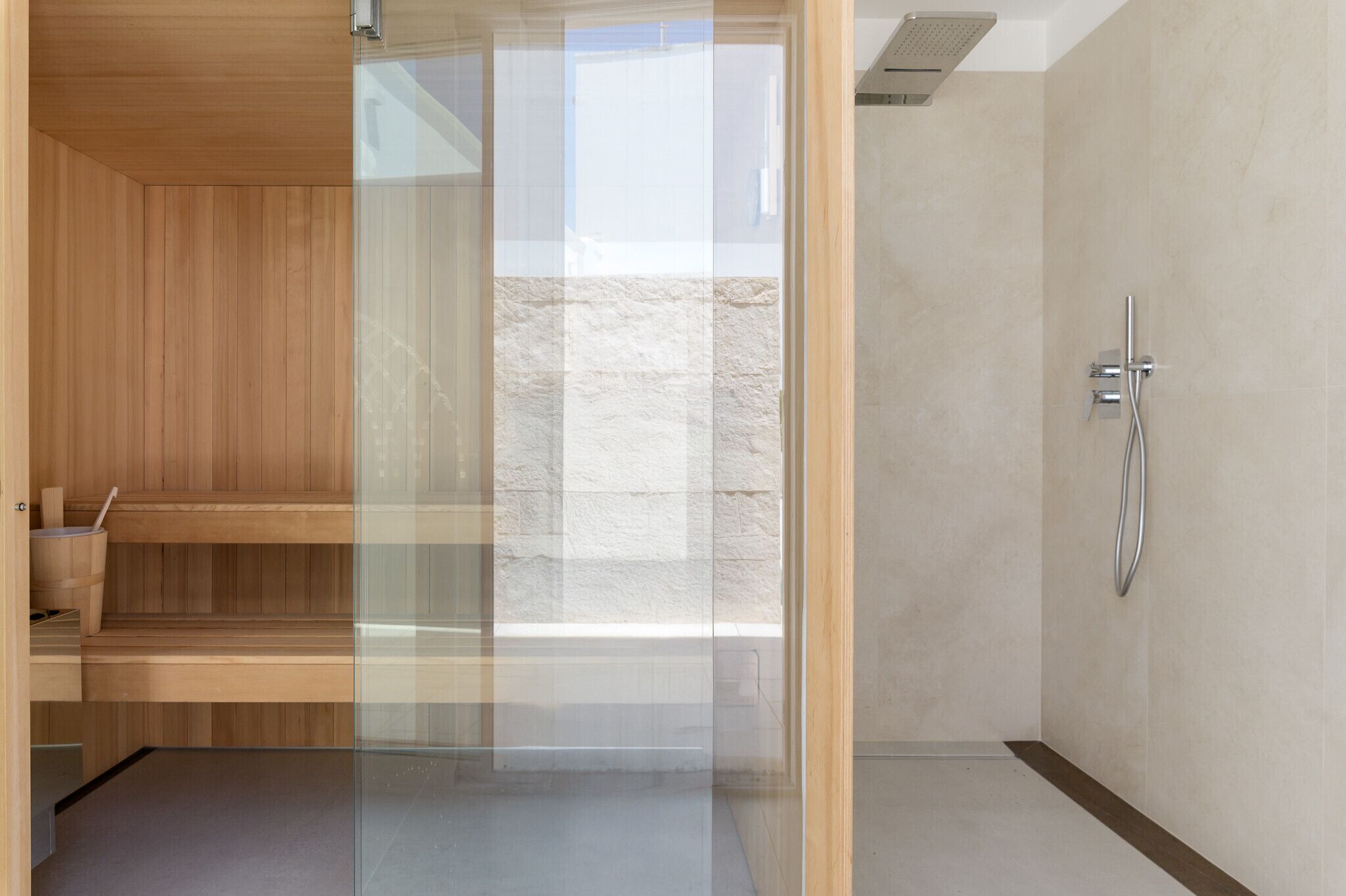 A modern bathroom with a wooden sauna, a glass shower enclosure, and a marble-tiled shower area.