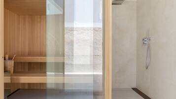 A modern bathroom with a wooden sauna, a glass shower enclosure, and a marble-tiled shower area.