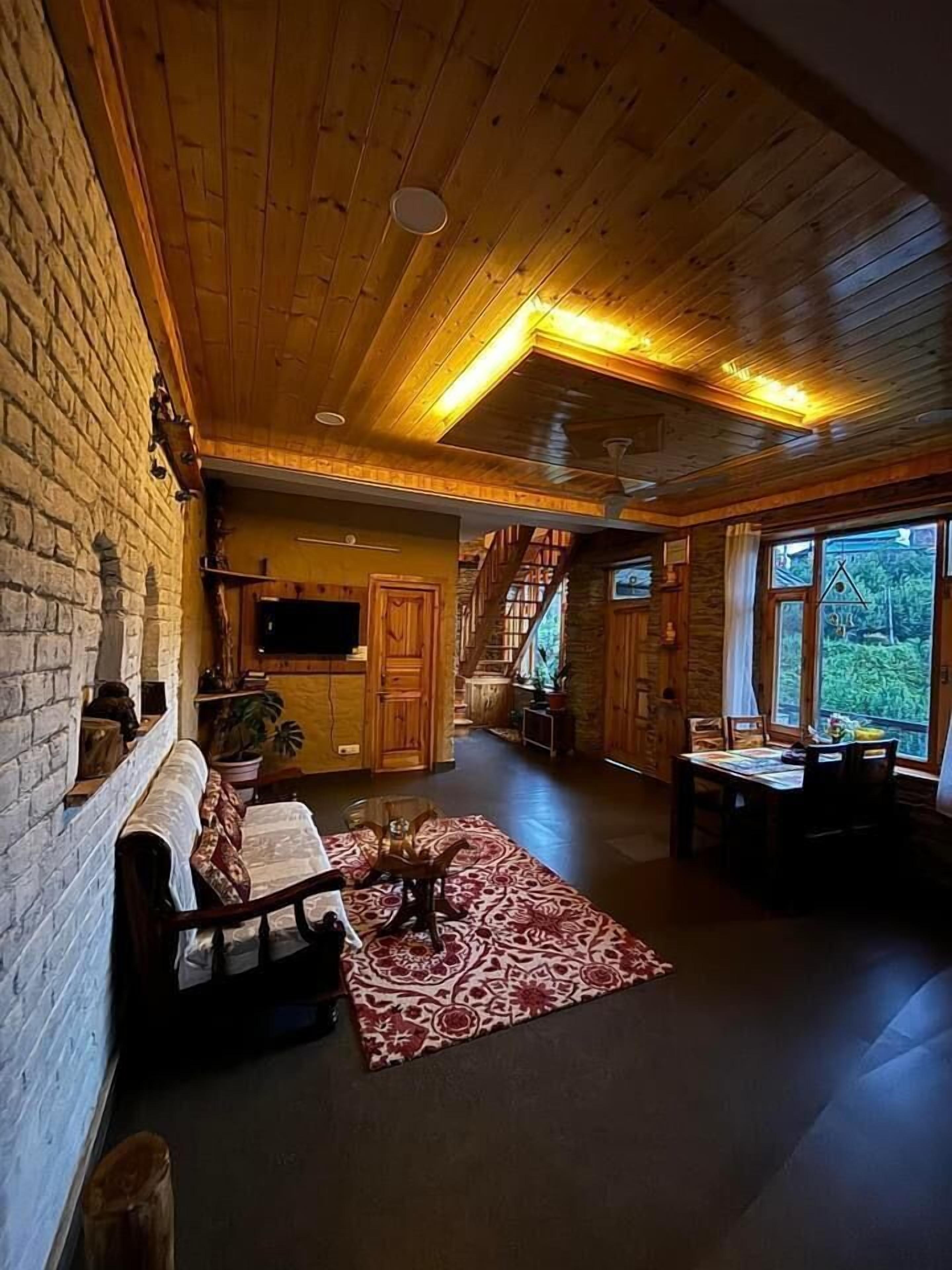 Amplia sala de estar con techo de madera, chimenea, sofá, mesa de comedor y escalera que sube a otro nivel.