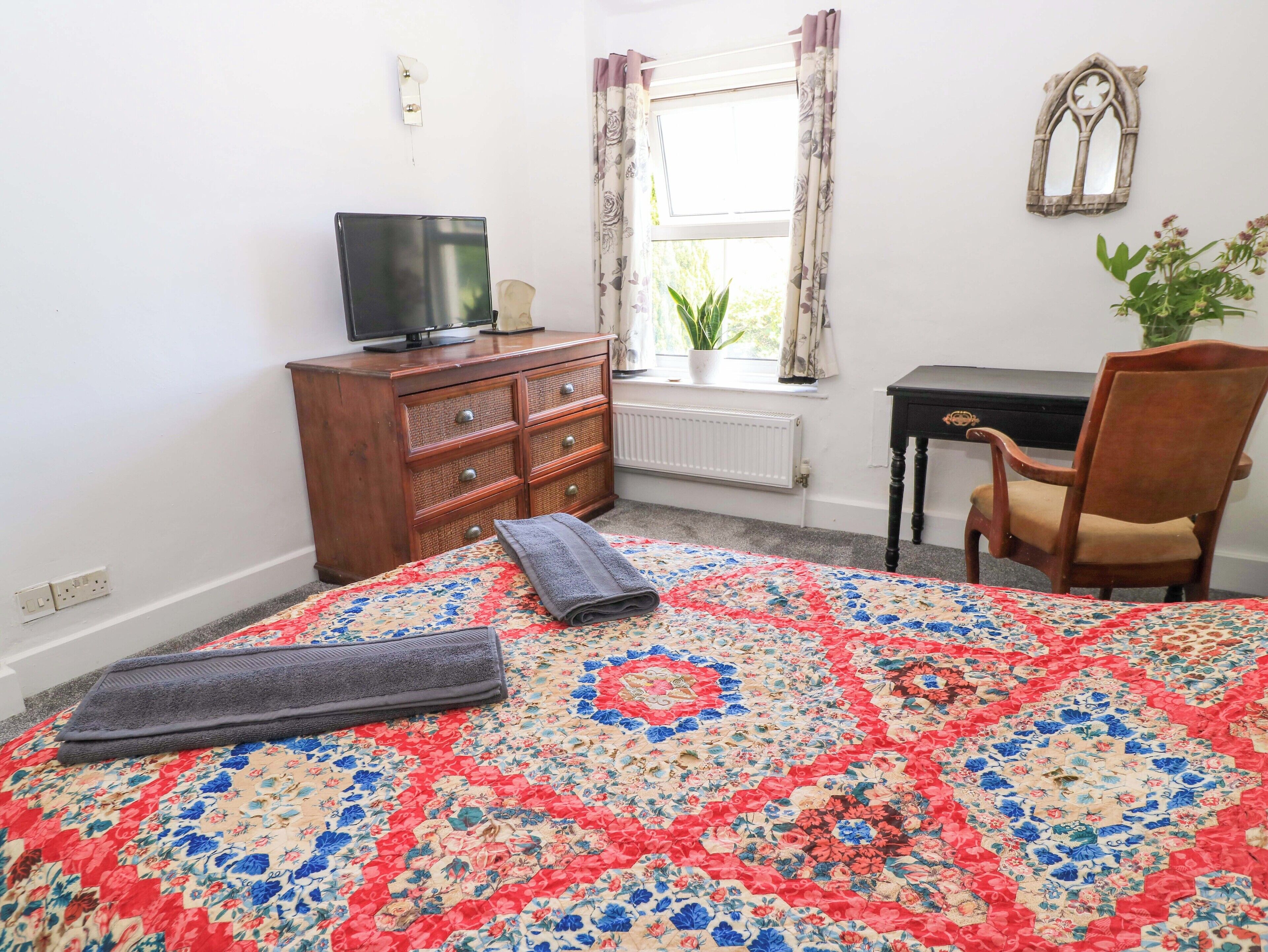 A bedroom with a bed, a dresser, a TV, a chair, a window with curtains, and a plant.