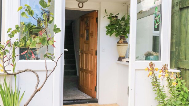 A doorway leading to a hallway with a wooden door, a tiled floor, and potted plants on either side.