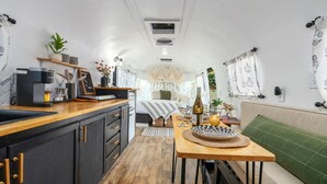 Een compacte, goed verlichte keuken met een koffieapparaat, een houten aanrecht en een eethoek met een tafel gedekt voor twee personen.