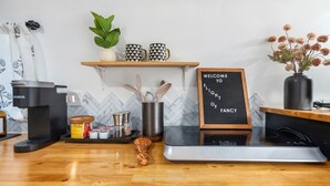 Een aanrecht met een koffieapparaat, een bordje met de tekst 'WELCOME TO FLIGHT OF FANCY', een plant en een vaas met gedroogde bloemen.
