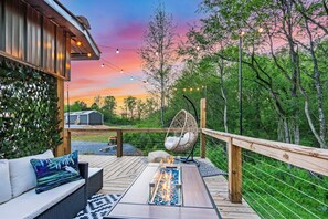 A deck with outdoor seating, a hanging chair, and a fire feature.