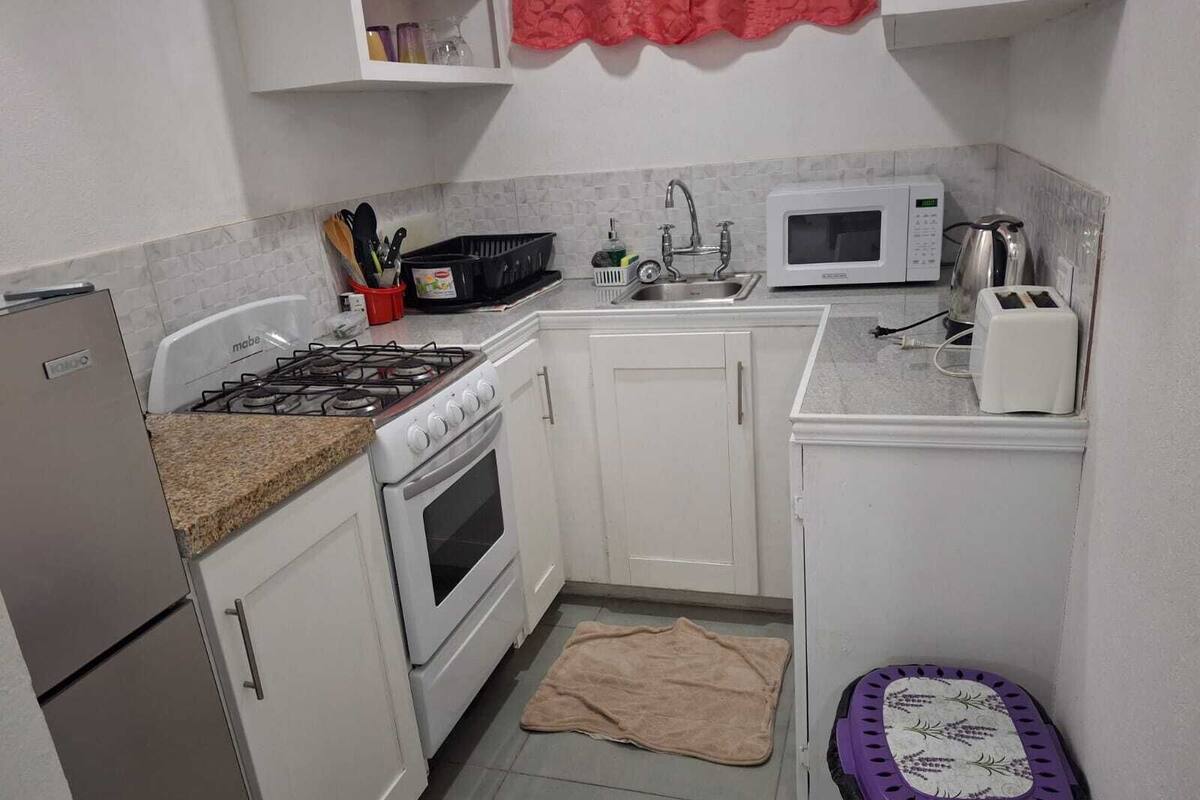 Une cuisine de taille réduite avec des meubles blancs, une cuisinière à gaz, un four à micro-ondes et un grille-pain.