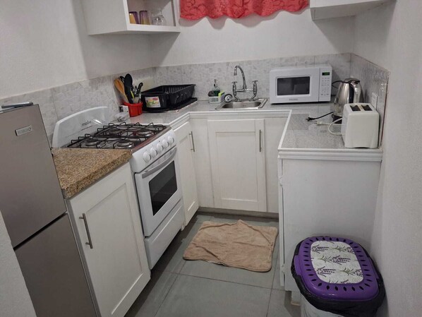 A compact kitchen with white cabinets, a gas stove, a microwave, and a toaster.