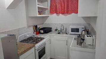 Uma cozinha compacta com armários brancos, fogão a gás, micro-ondas e torradeira.