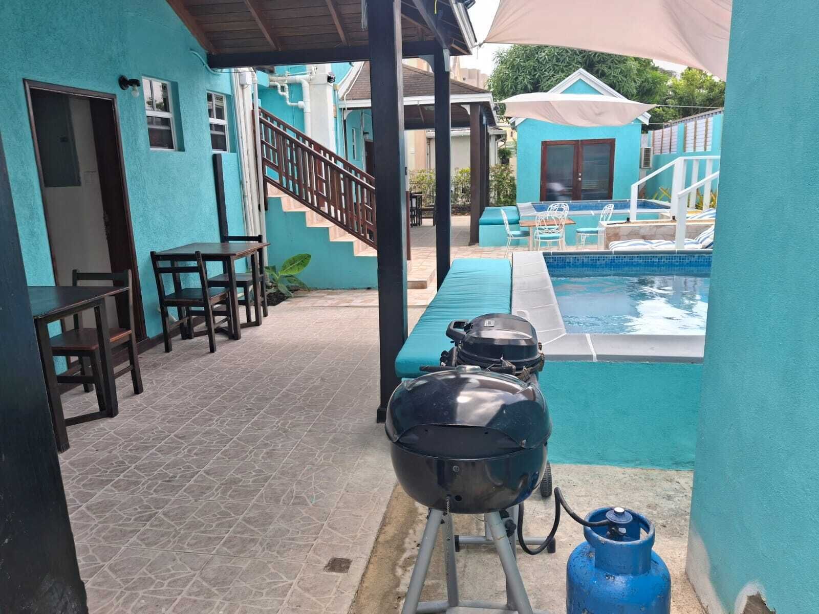 Zona de piscina con una parrilla, asientos al aire libre y una escalera que conduce a un edificio.