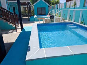 A swimming pool with a blue tiled edge, a wooden bench, and a small house-like structure in the background.