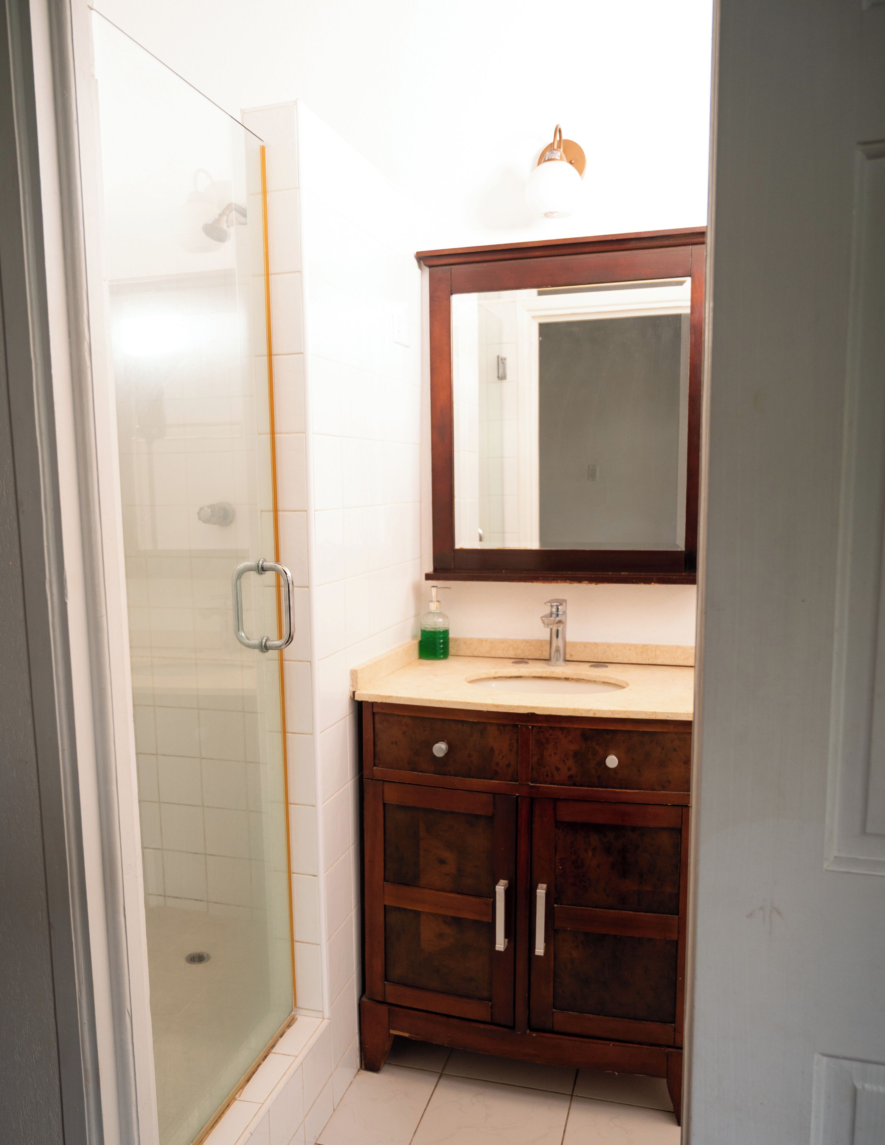 A bathroom with a glass shower enclosure, a wooden vanity with a mirror, and a sink.