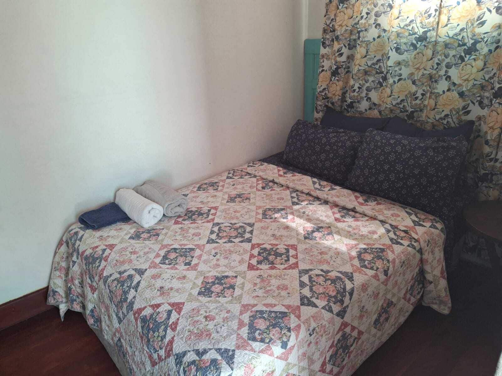 Una cama bien hecha con un colcha floral, dos toallas enrolladas y una cortina estampada con flores.