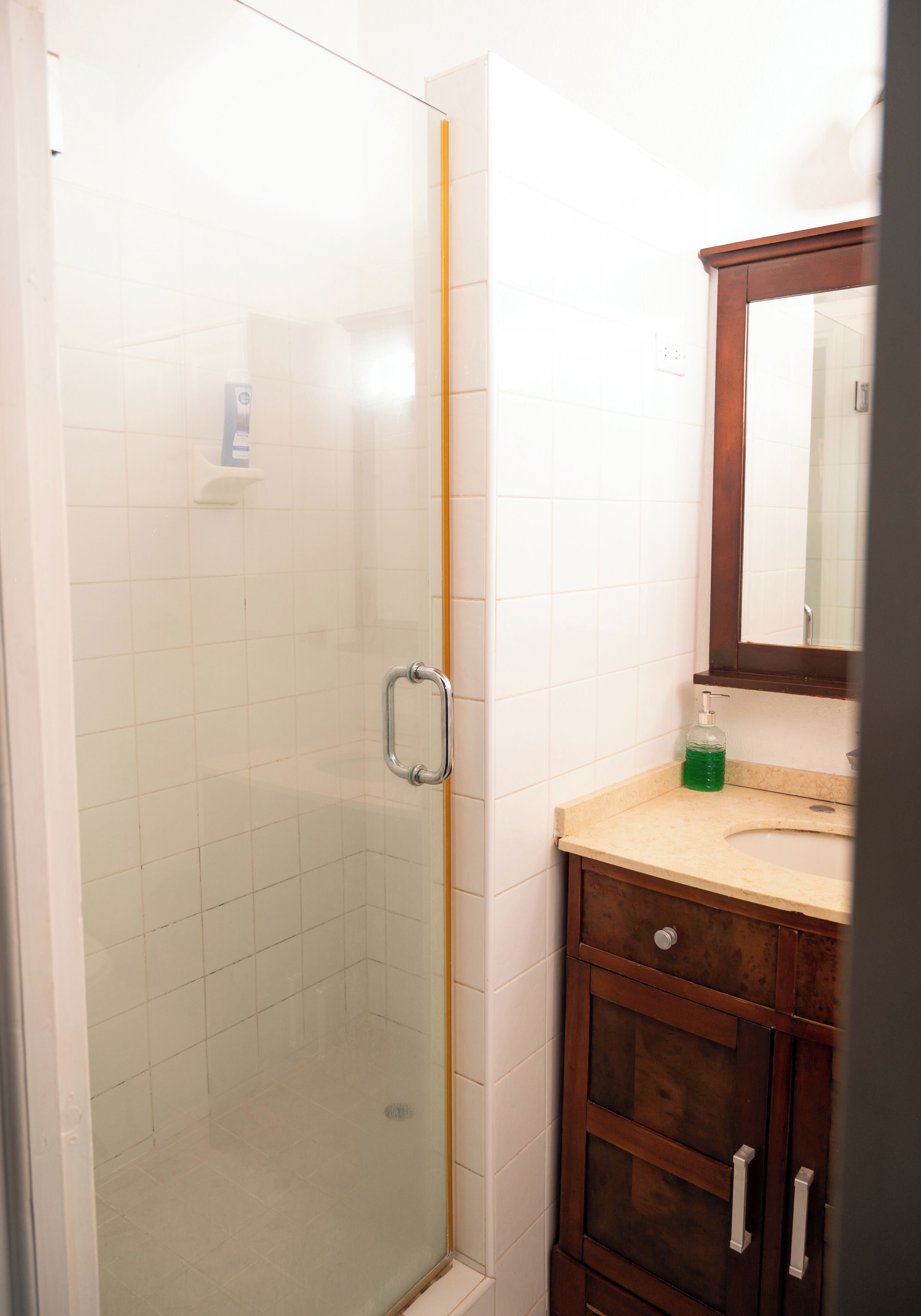 A bathroom with a glass shower enclosure, a wooden vanity with a mirror, and a sink.