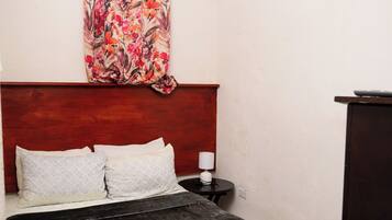 Un dormitorio con una cama, una mesita de noche, una lámpara, una cortina con estampado floral y un equipo de aire acondicionado.