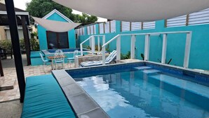 Une piscine dont le bord est recouvert de carreaux bleus, entourée d’un patio abrité avec des sièges et une petite table.