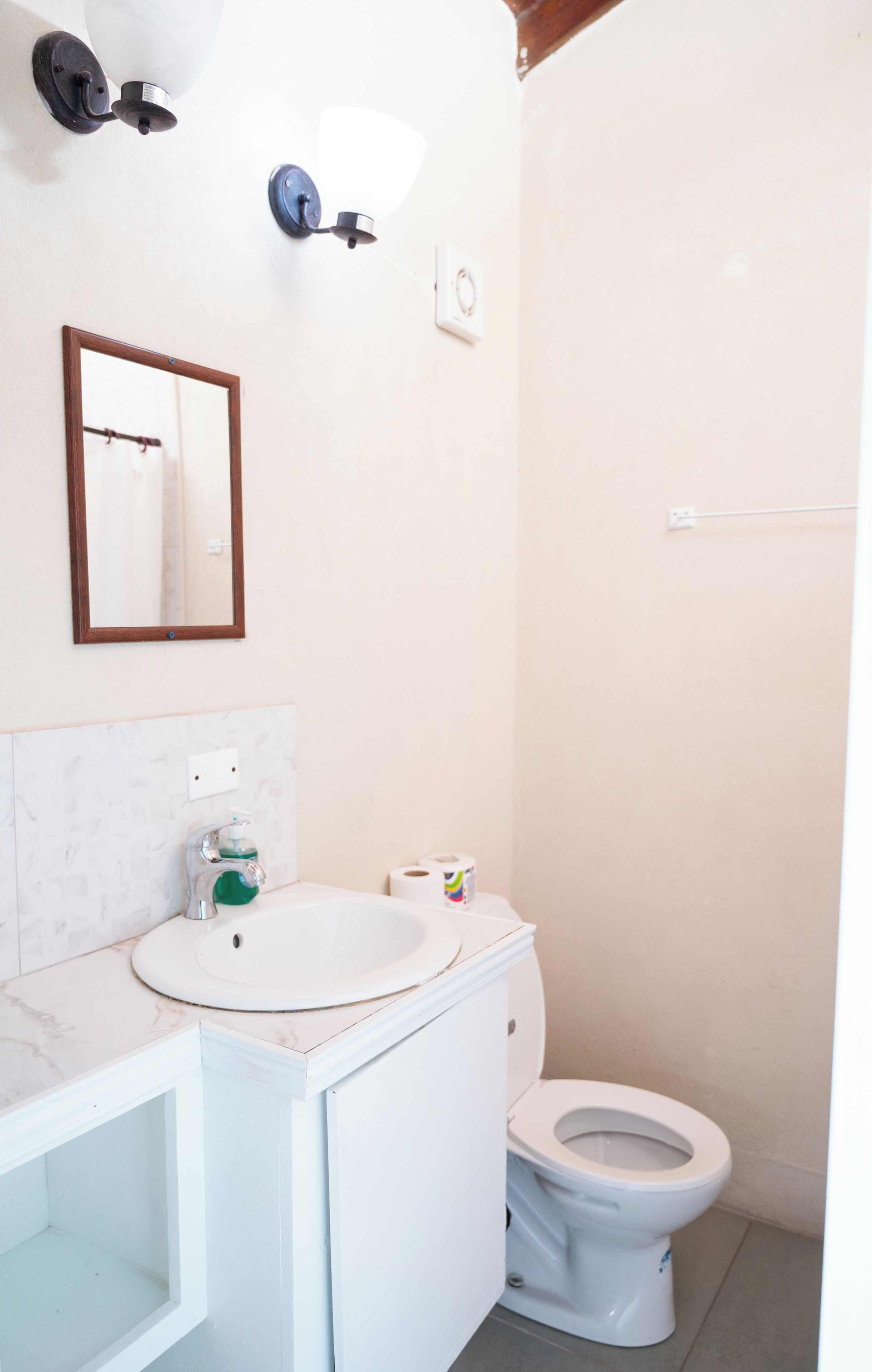 Un baño con lavamanos blanco, espejo, inodoro y toallero.