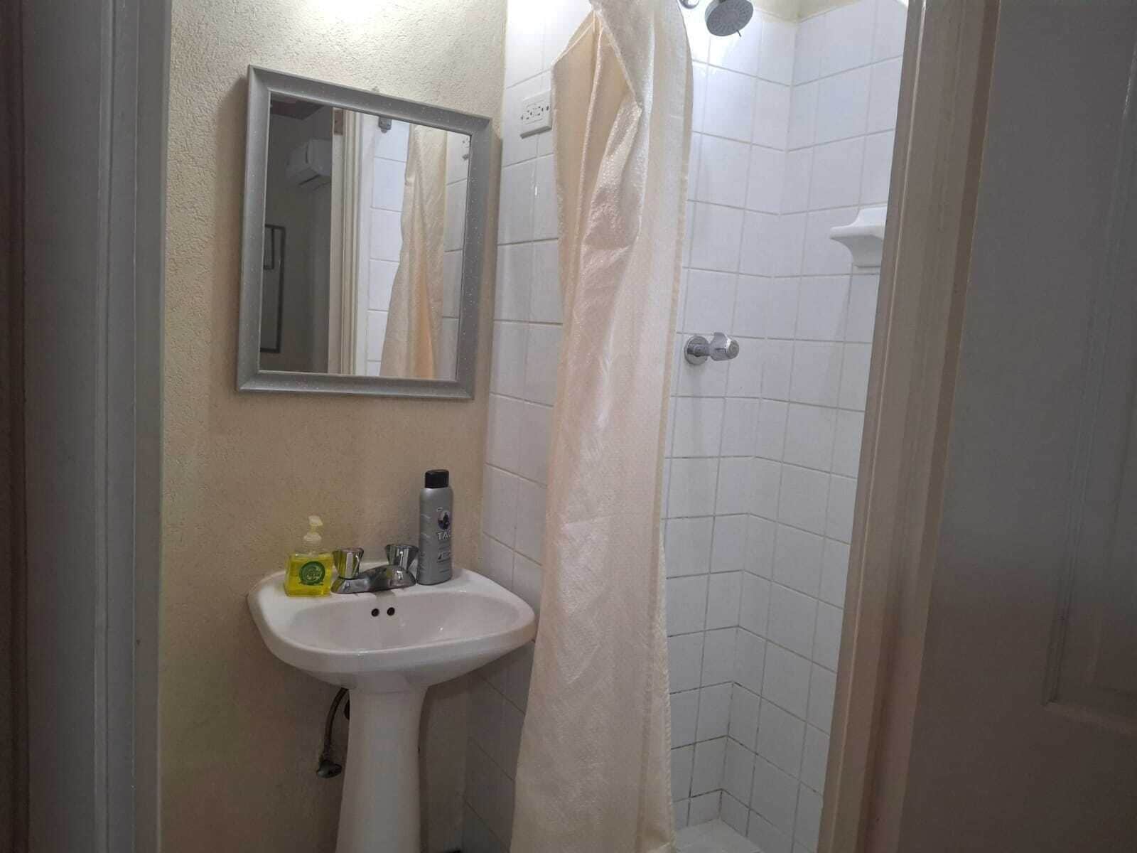 Un baño con lavamanos blanco, espejo y zona de ducha.