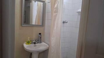 Un baño con lavamanos blanco, espejo y zona de ducha.