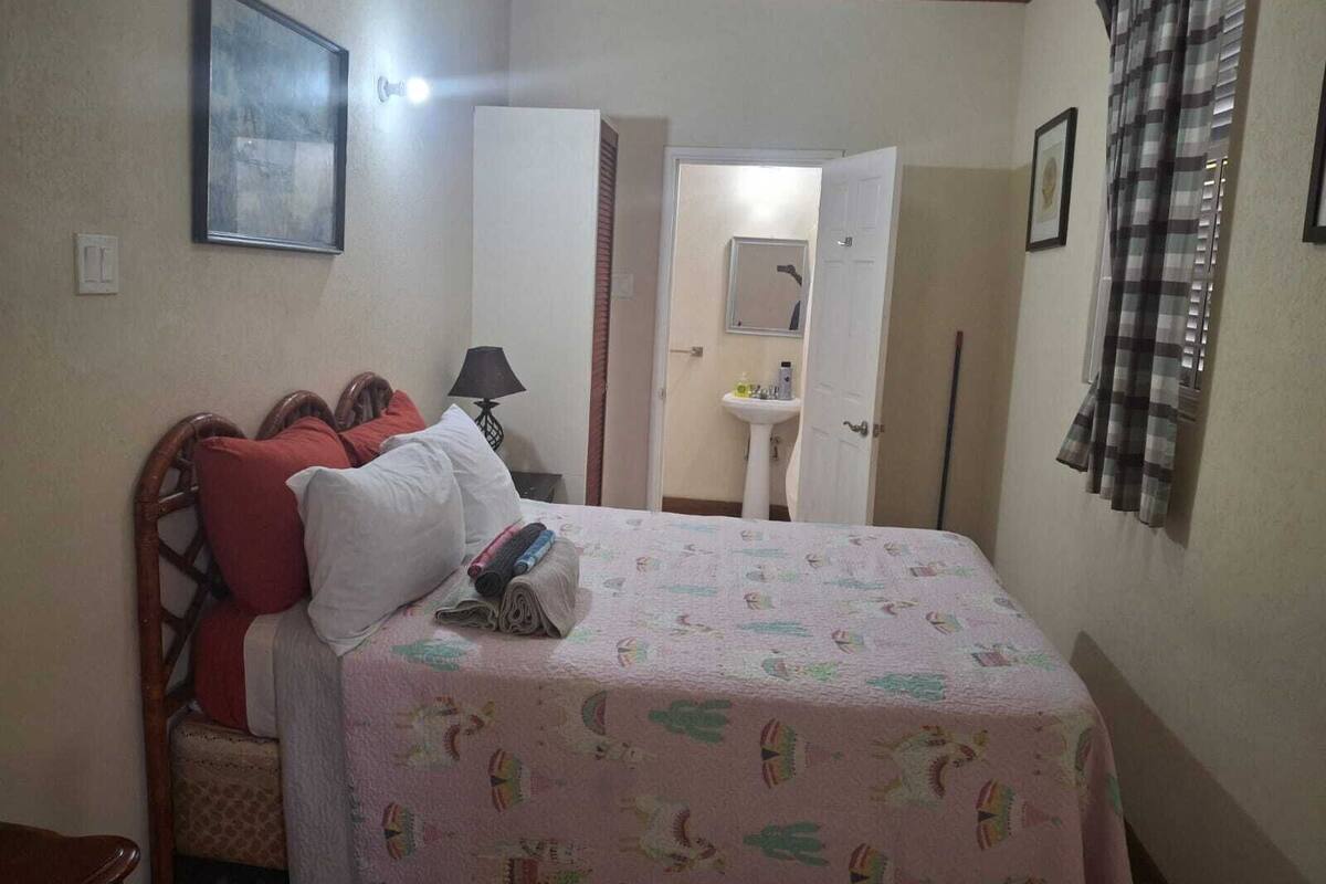 Une chambre à coucher avec un lit, une table de chevet, une lampe, un miroir et une fenêtre avec des rideaux.