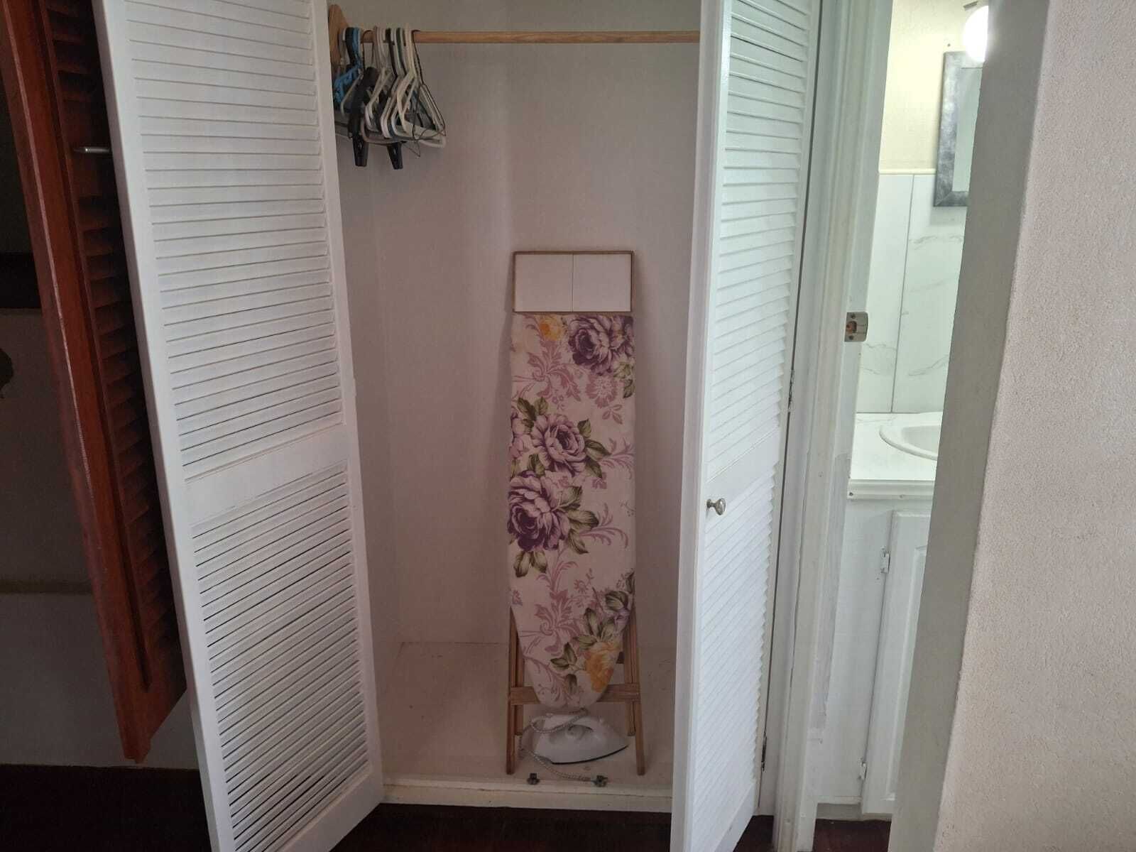 A walk-in closet with a wooden hanger rod and a floral-patterned shelf.