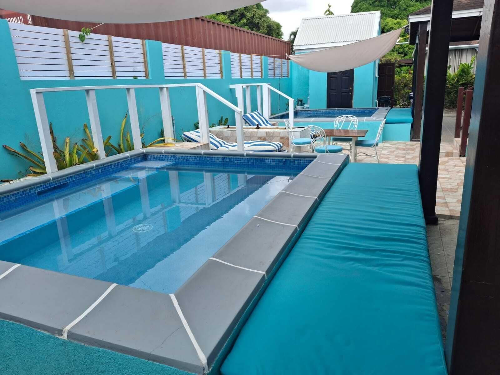 Una piscina con borda piastrellata blu, un solarium bianco e un'area salotto coperta con cuscini azzurri.