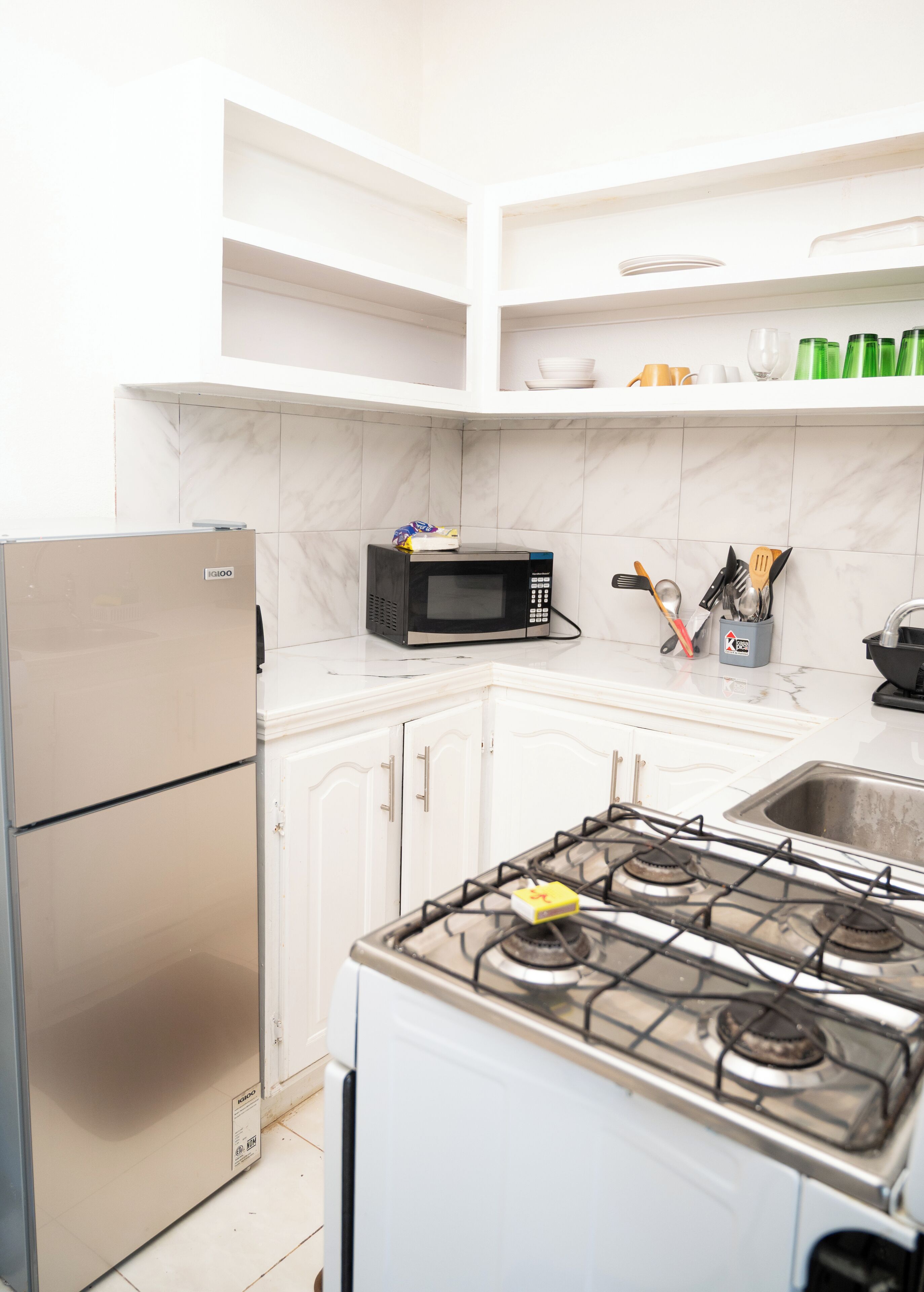 Una cocina equipada con refrigerador, microondas, estufa y estantes con utensilios de cocina.