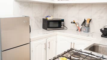 Una cocina equipada con refrigerador, microondas, estufa y estantes con utensilios de cocina.