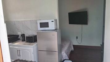 A compact kitchen with a gas stove, a microwave, and a refrigerator. A television is mounted on the wall.