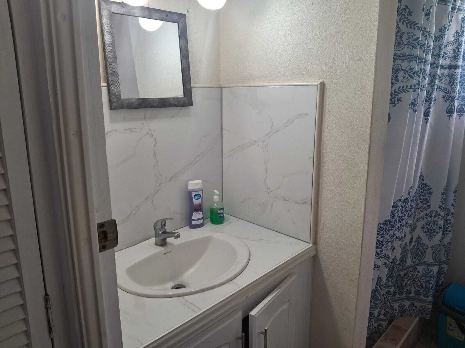 Un baño con lavamanos blanco, un espejo y cortina de ducha.
