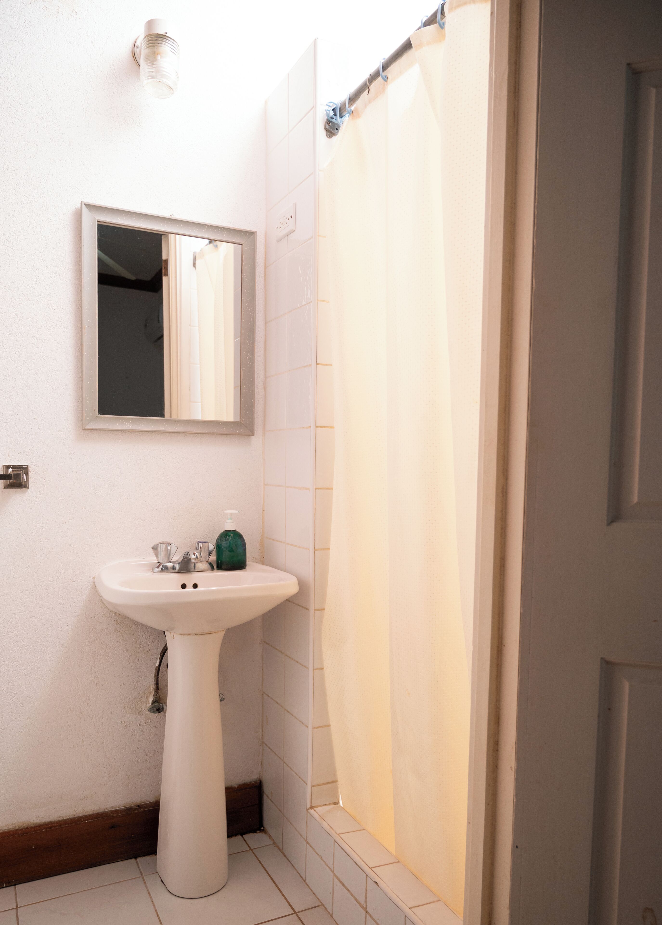 Une salle de bain avec un lavabo blanc, un miroir et un rideau de douche.